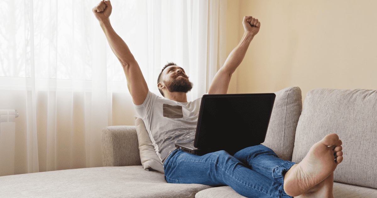 man on sofa with laptop and arms raised high