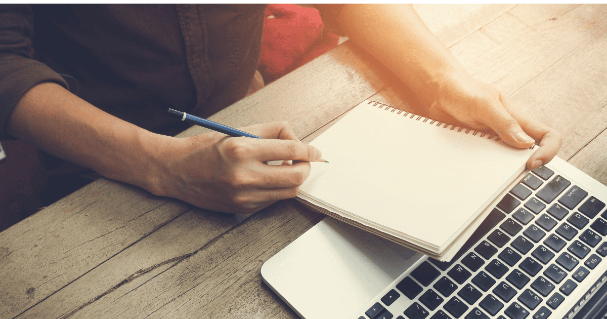 man writing in notebook with laptop on the table