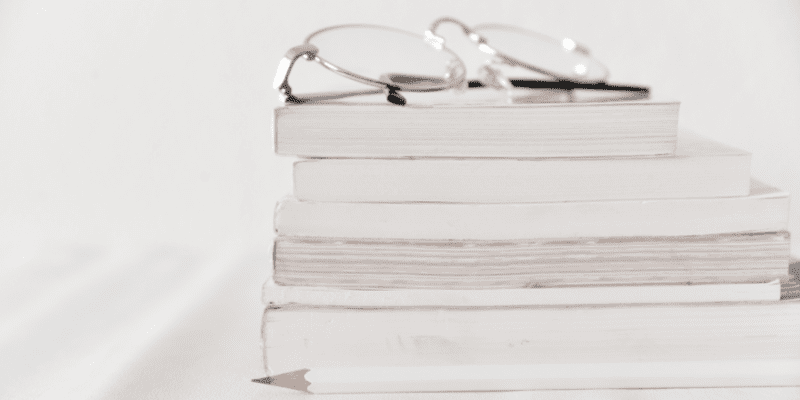 Stack of books with eyeglasses on top and pencil white background.