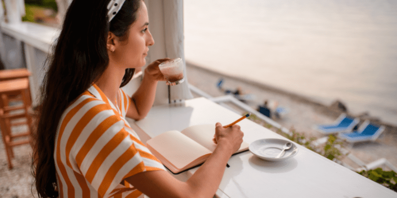 woman writing at window drinking coffee.